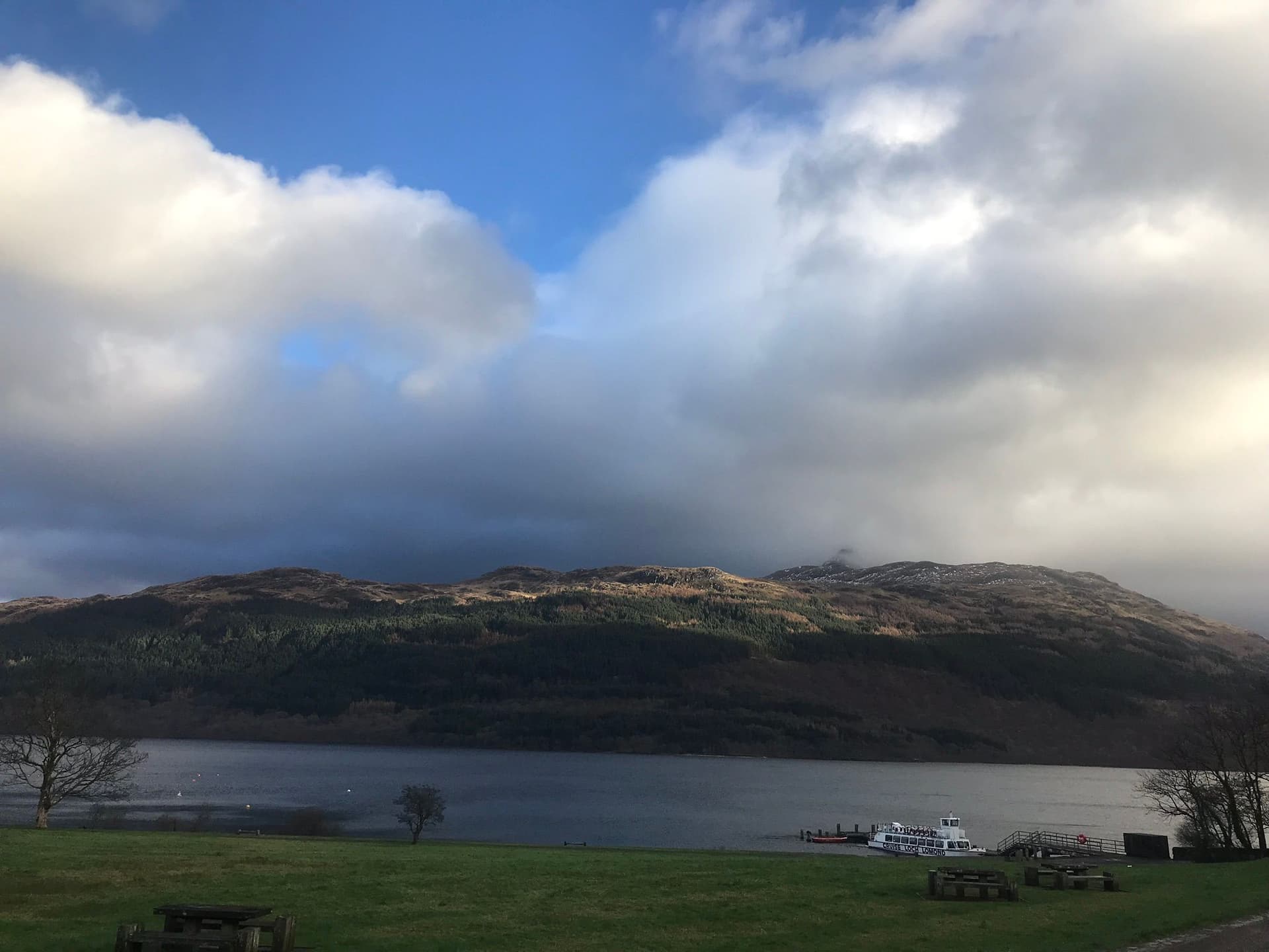 A scenic view of a loch surrounded by mountains, framed by a lush grassy field in the foreground.