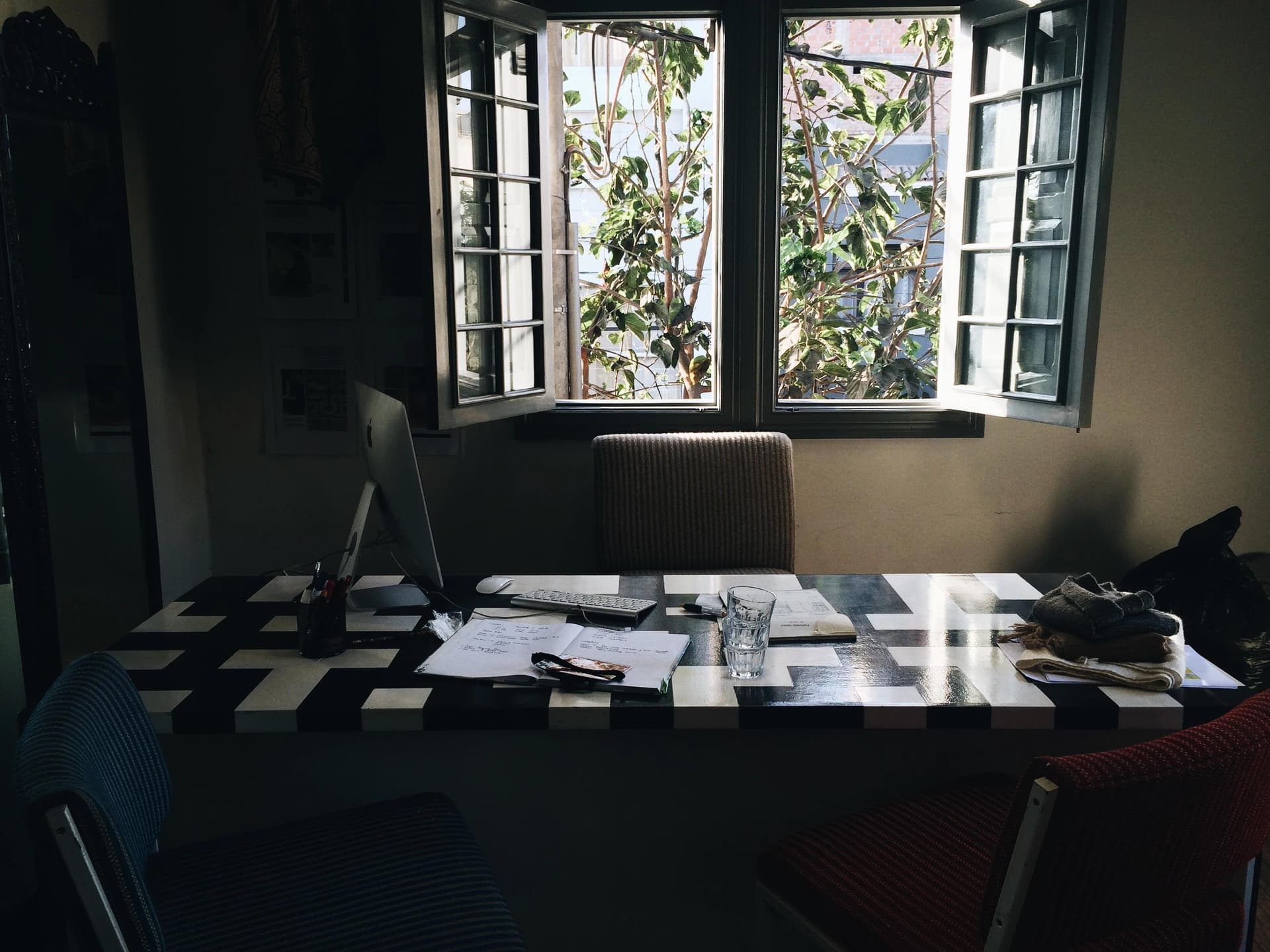A cozy workspace with a checkered desk, an iMac, papers, and an open window revealing greenery outside.