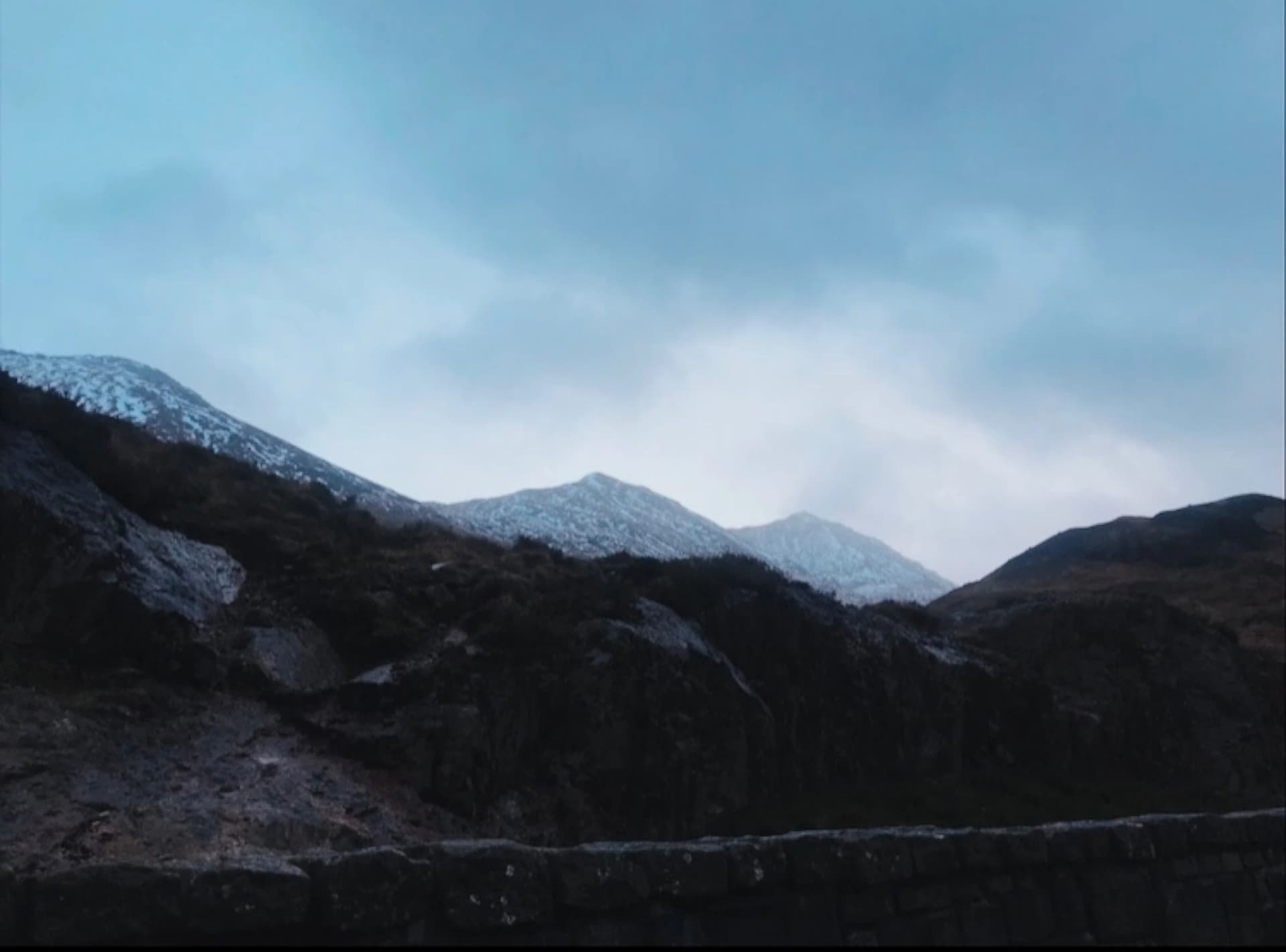 A dramatic mountain range under a dark sky, featuring a prominent peak in the background.