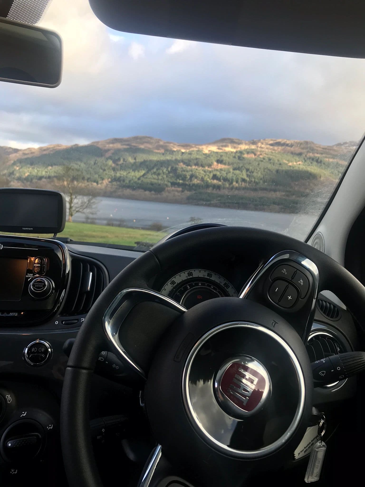 A car dashboard is prominently displayed, with a serene lake visible in the background, enhancing the tranquil atmosphere.